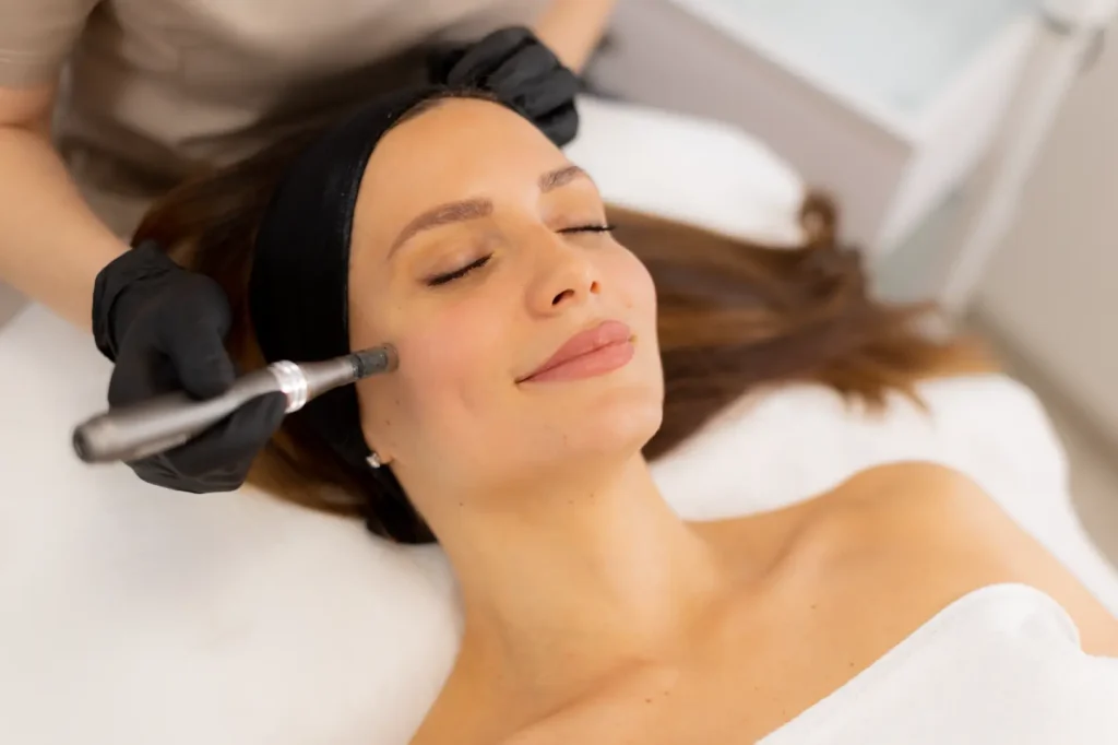 Woman reclines with eyes closed while a practitioner applies a handheld device to her cheek.