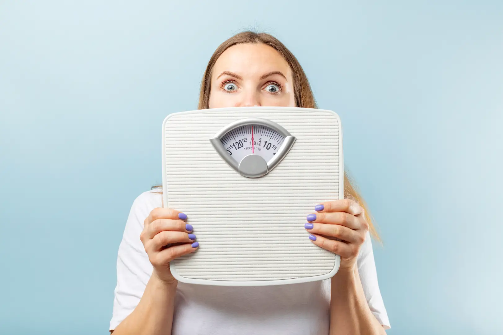 Woman holds a mechanical bathroom scale in front of her face against a light blue background.