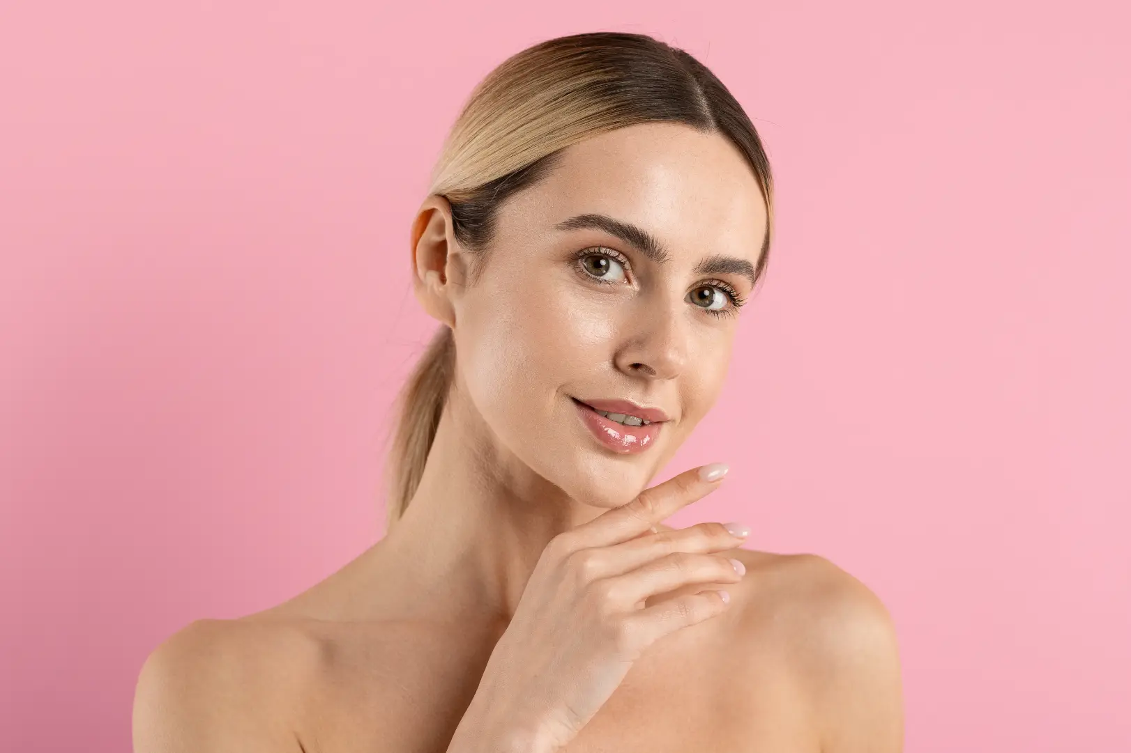 Woman poses with one hand beneath her chin against a solid pink background.