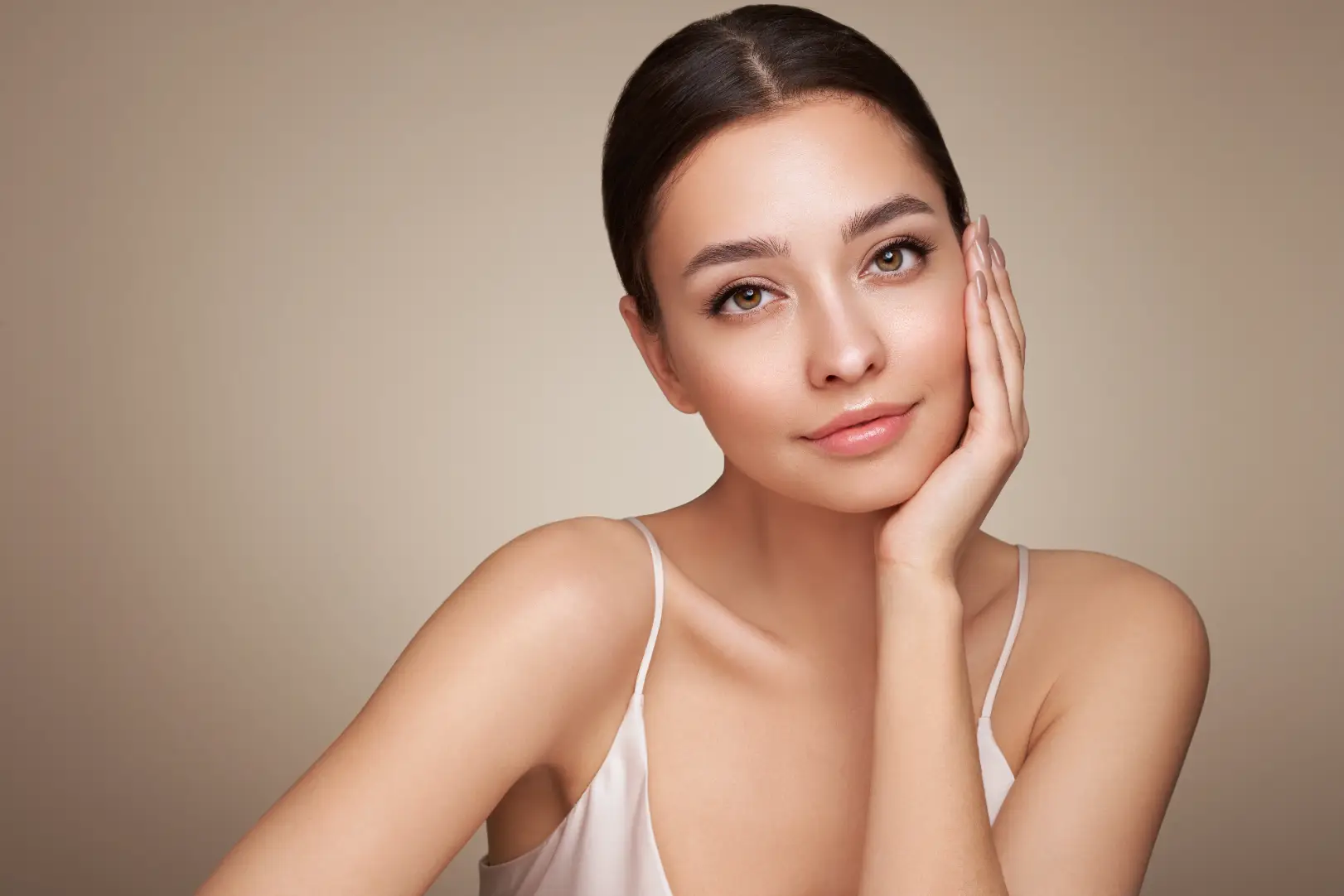 Woman rests one hand against her cheek while looking toward the camera against a beige background.
