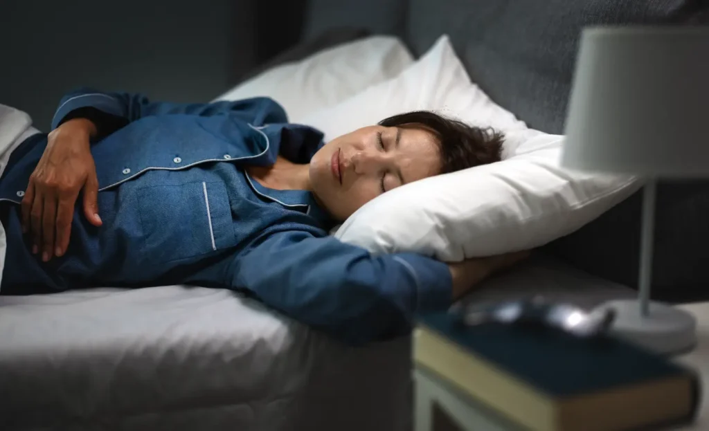 Woman wearing blue pajamas sleeping on her side in bed with her head resting on a white pillow.